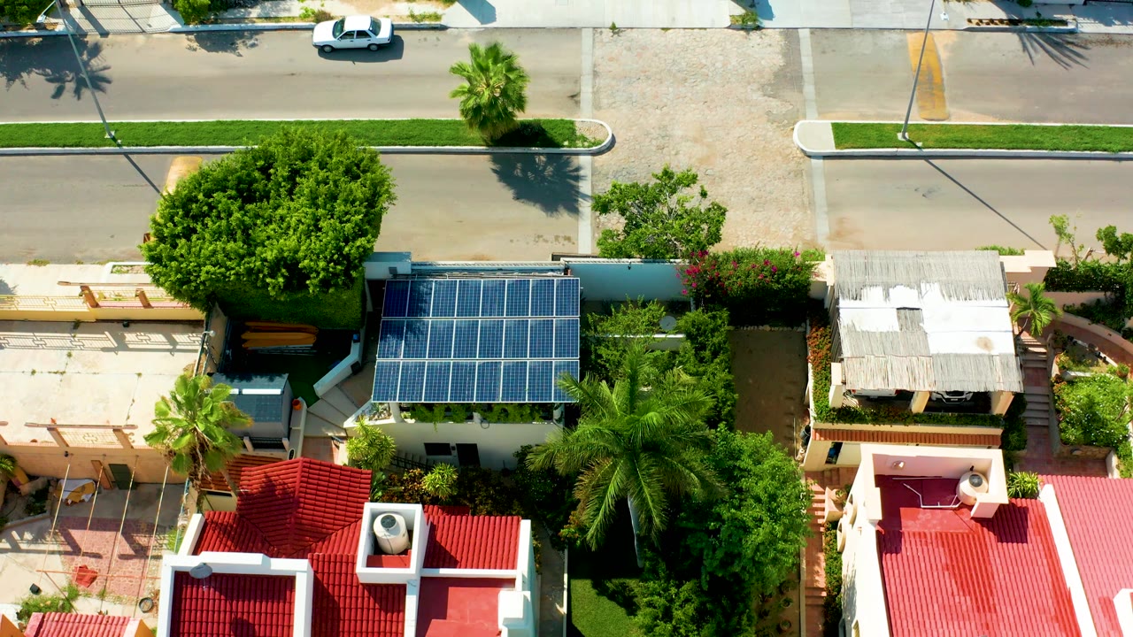 Overhead neighborhood view with solar panels, red roofs, and the white car near the road edge.