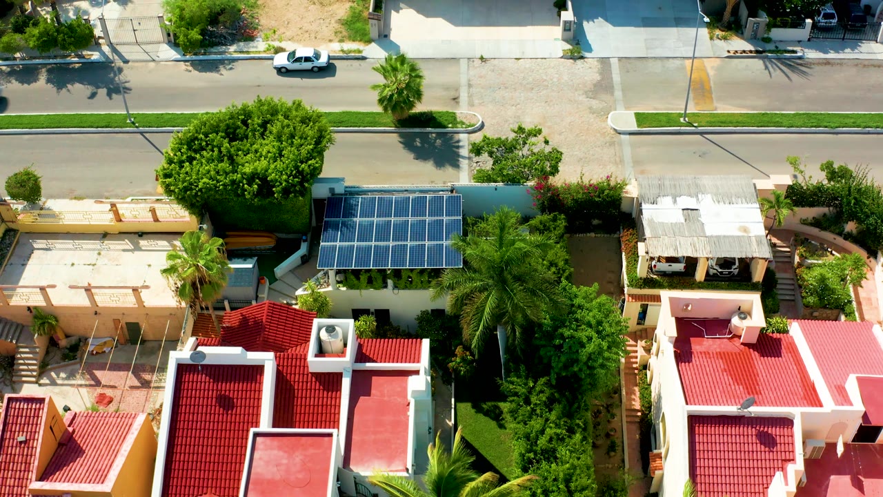 Aerial residential street scene with red rooftops, solar panels, palms, and a white car.