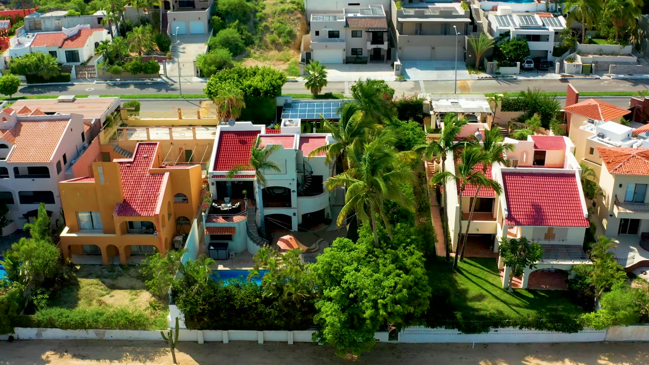 Aerial view over stucco homes, palm trees, blue pools, and solar panels