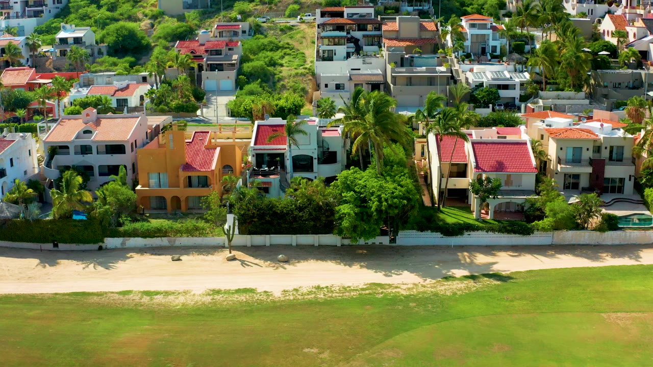 Aerial view of San Jose Del Cabo beachfront residences with palm shadows stretching across the sand and no visible people.