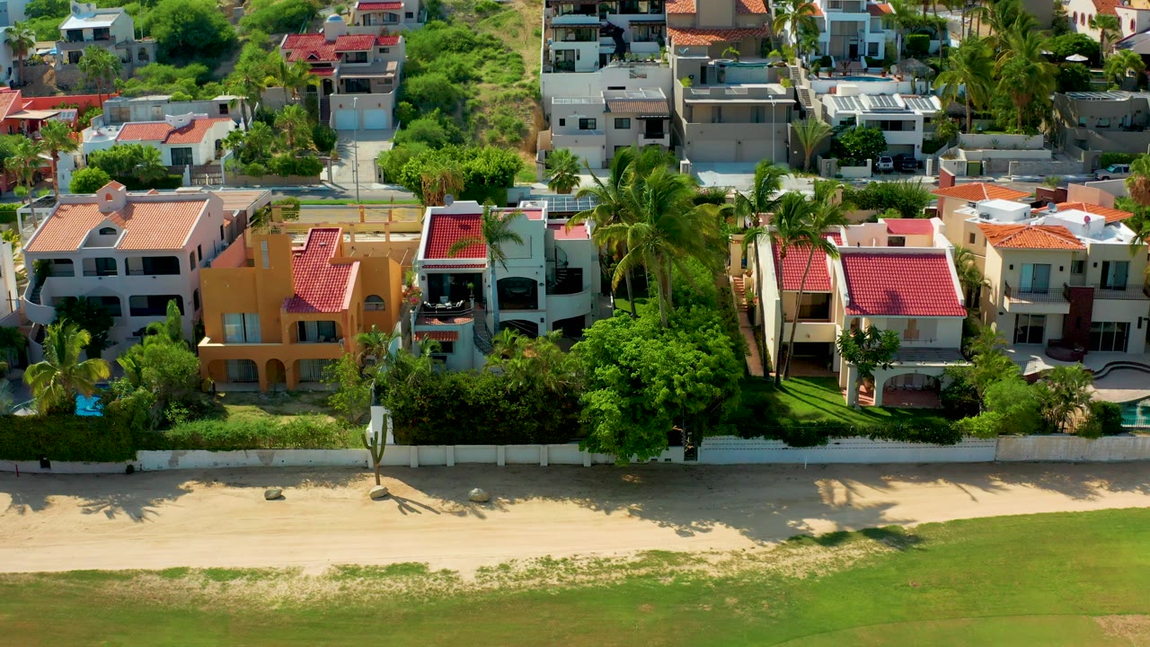 Beachfront homes and palms viewed from above with sand and water below.