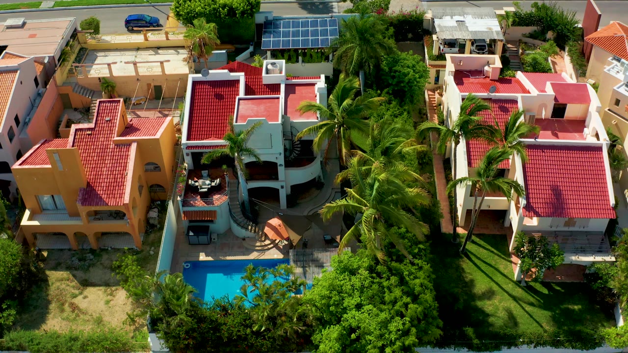 Overhead neighborhood frame with pool, red roofs, palms, and garden walls.