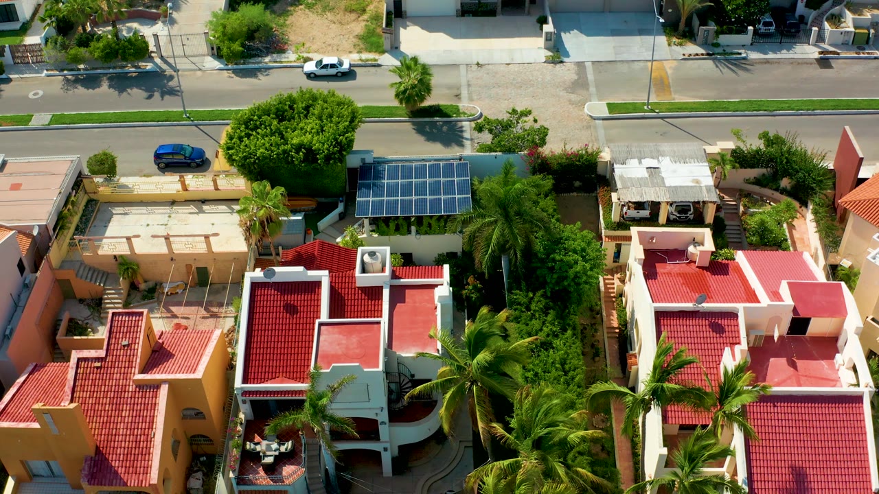 Overhead view of red-roof houses, solar panels, palms, and street traffic