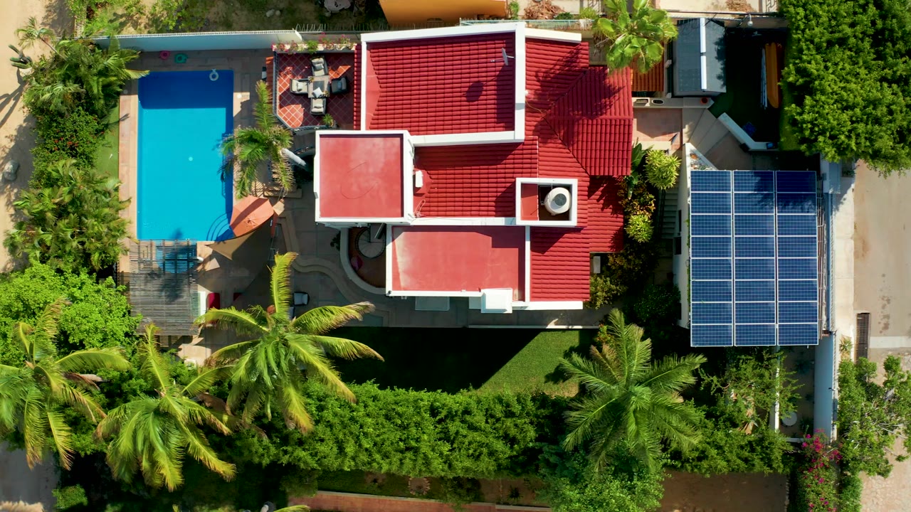 Aerial view of pool beside a red-roofed home and solar panel array.