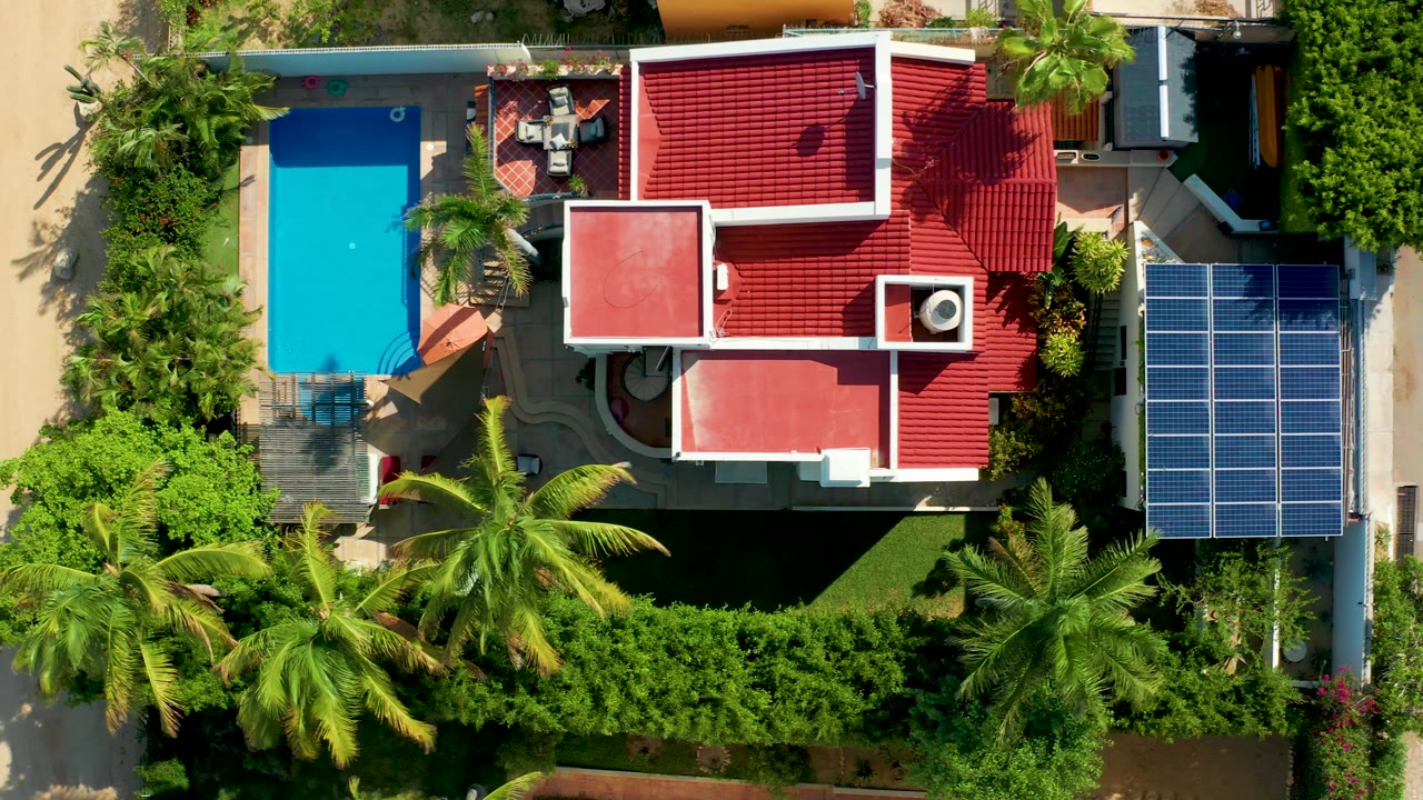 Overhead residential property with pool, palms, red roof, and solar panels.