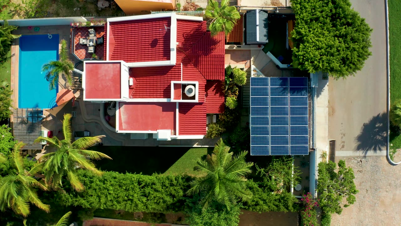 Overhead frame of a red-roofed home, pool, solar panels, driveway, and road edge.