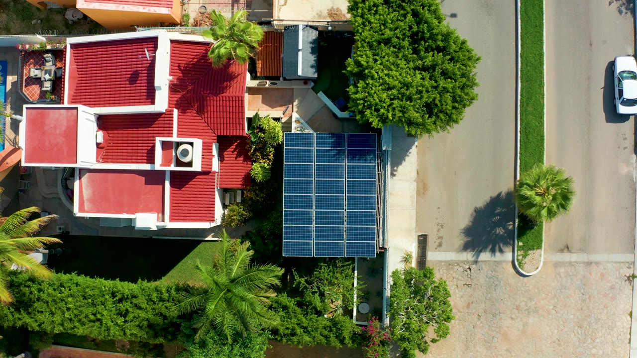 Top-down view of house, solar panels, road, trees, and white car.