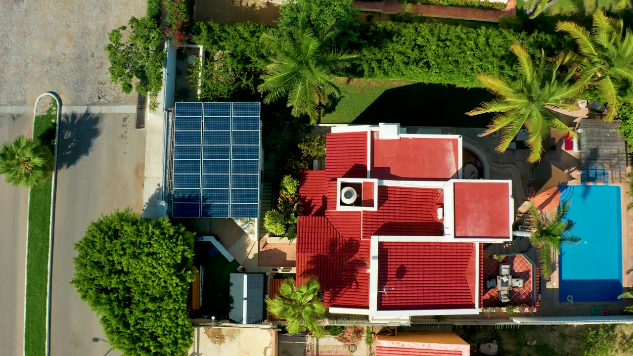 Overhead residential property with red roofs, solar panels, street, palms, and pool.