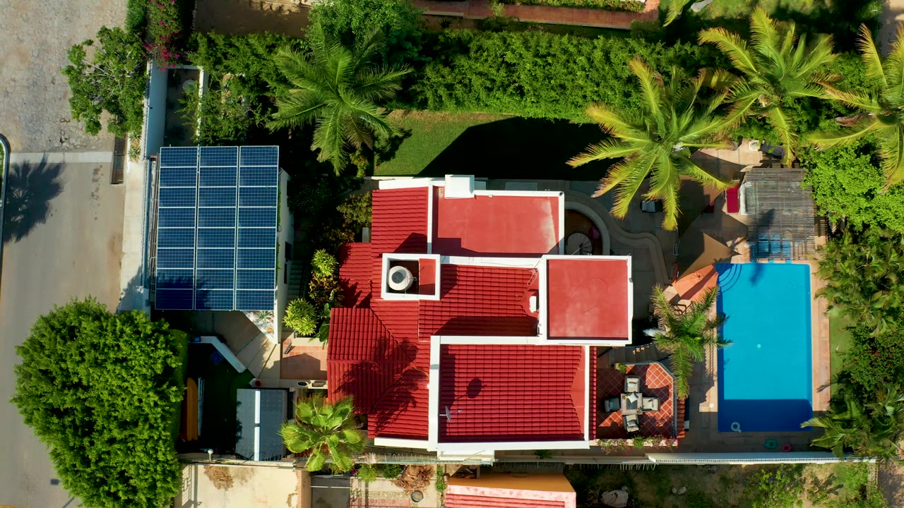 San Jose del Cabo overhead frame showing the red roof home slightly shifted in view, with the solar panels, pool, street border, palms, and no visible people.