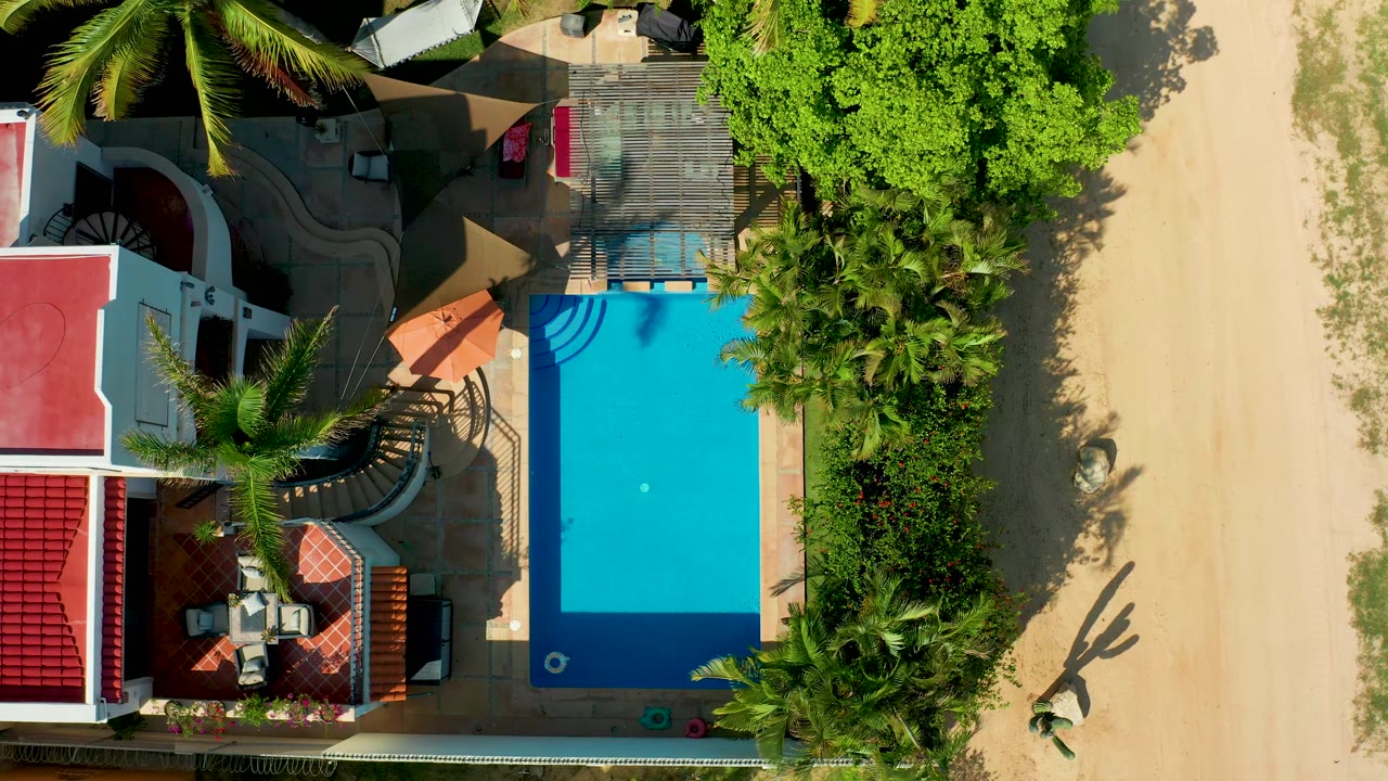 Blue pool with cover partly removed beside palms and a white house.