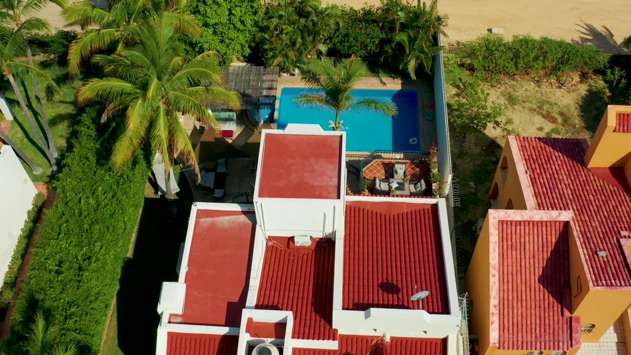 Aerial residential view with palm canopy, pool, and red tiled roofs.