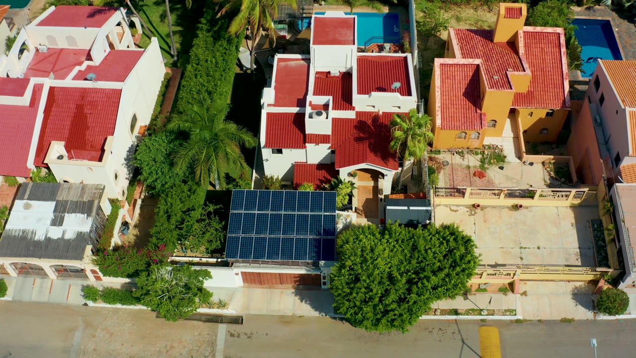 Drone overhead of residential roofs, palm canopy, solar panels, and road