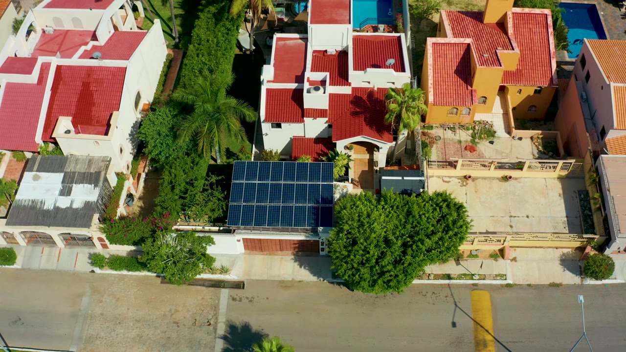 San Jose Del Cabo aerial view showing the solar panel roof closer to the lower center, red-roofed homes above it, dense greenery, and no visible people.