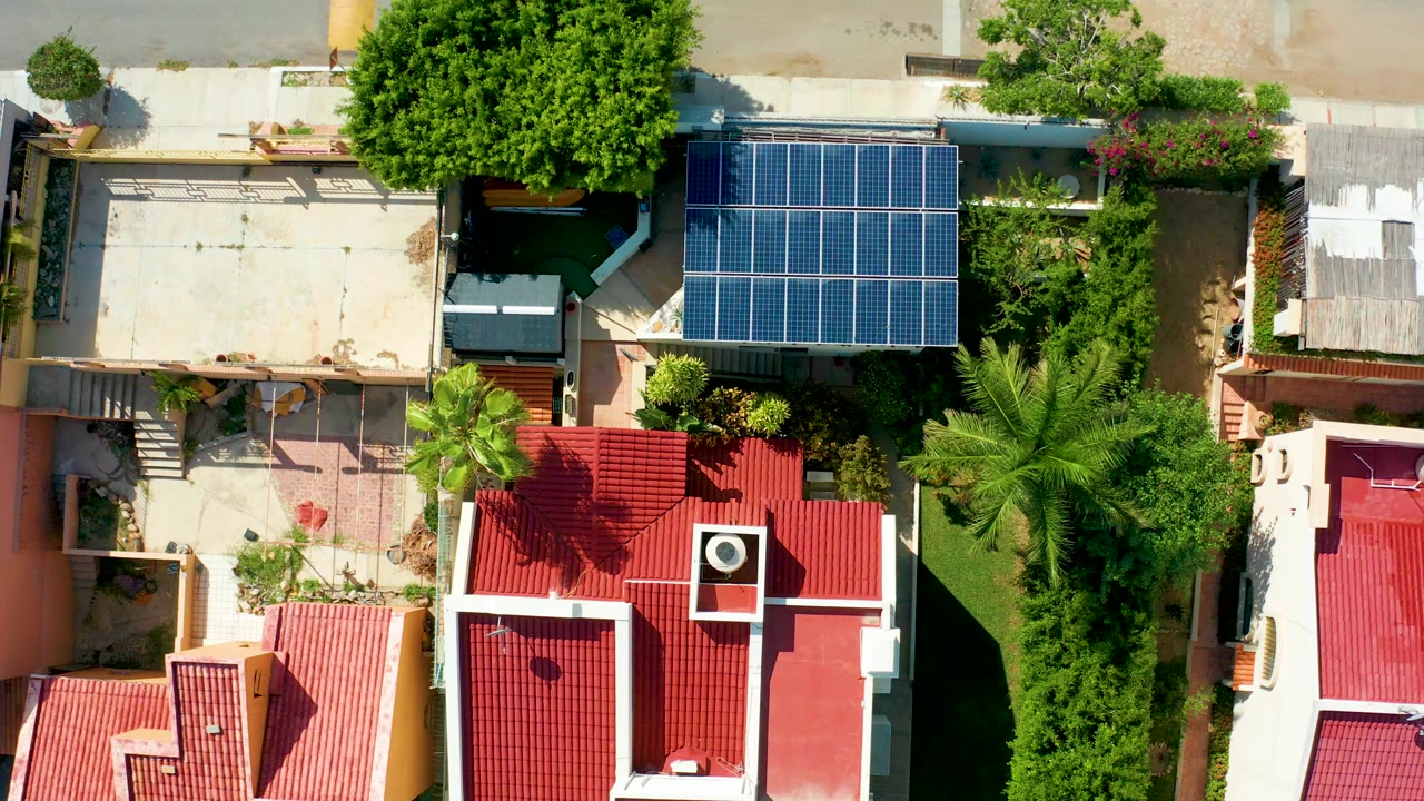 Top-down aerial frame over San Jose Del Cabo homes with red tile roofs, a blue solar panel array, palms, patios, and no visible people.