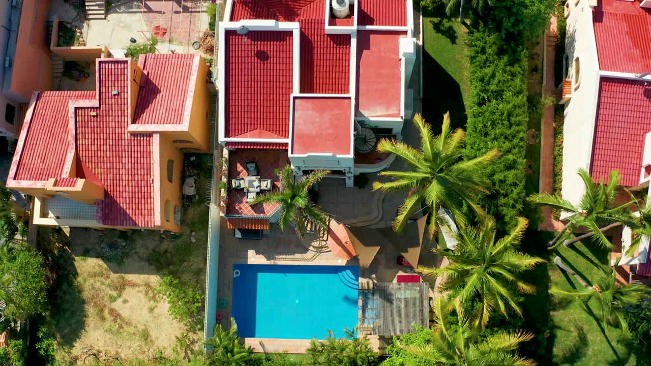 Aerial view of red roof houses with pool, palms, and surrounding greenery.