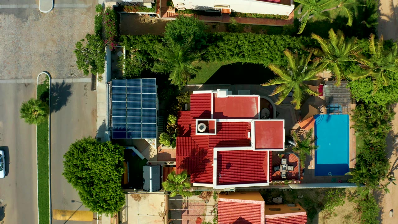 Overhead view of a residential property with pool and solar panels as a white car passes left.
