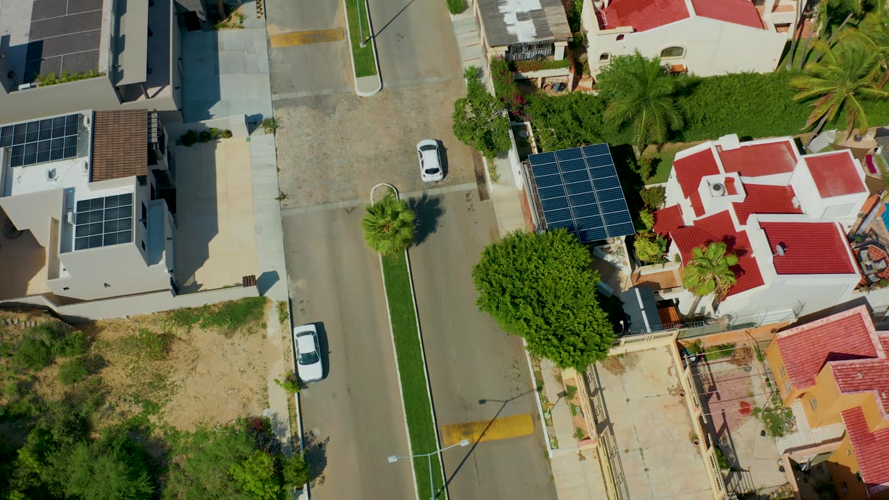 White car on a straight residential street with houses and a dry lot nearby.