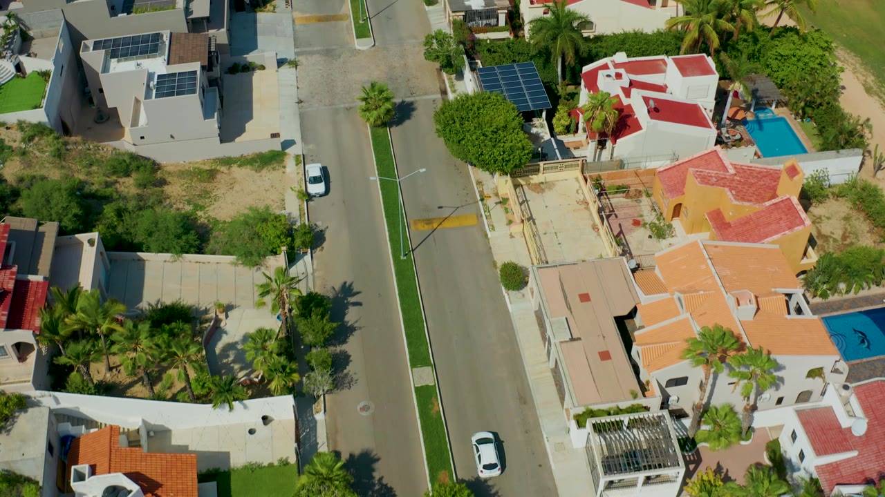 Overhead residential block with a road, homes, pools, and palm trees.