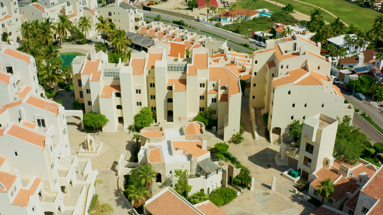 Aerial view of apartment-like buildings, courtyards, palms, and a pool.