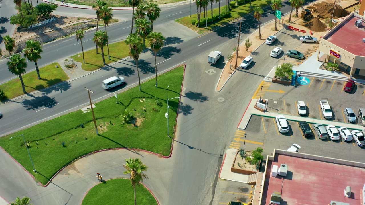 Aerial intersection view with a white truck and several cars near a palm-lined median.