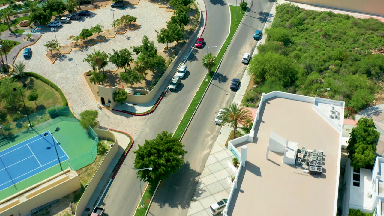 Aerial view of cars on a curved road near tennis courts and trees