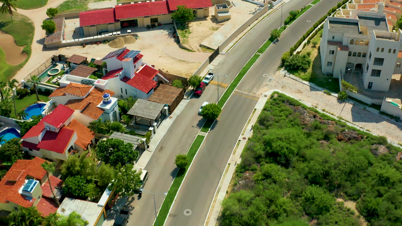Aerial residential block with a road, houses, pools, and greenery.