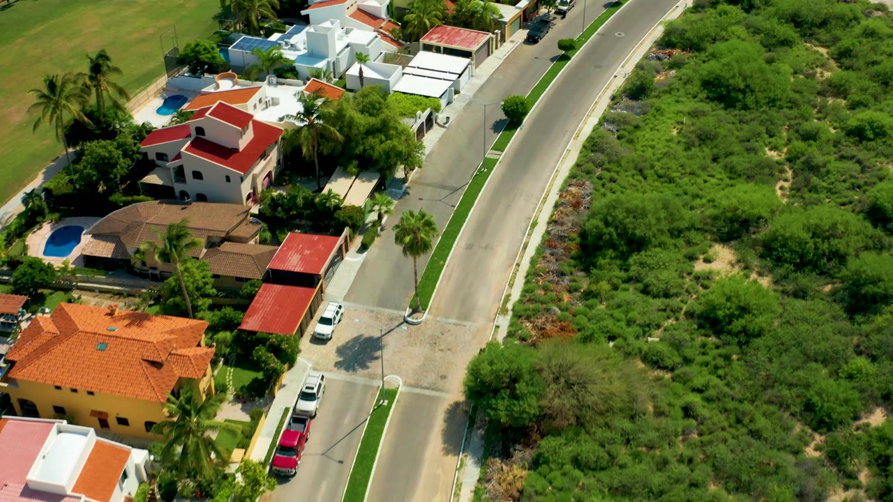 San Jose del Cabo aerial view with the road running through the right side of frame, residential houses and pools to the left, green brush to the right, and no visible people.