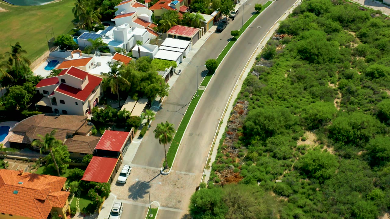 Aerial view of red-roofed houses beside a curved road and green open land.