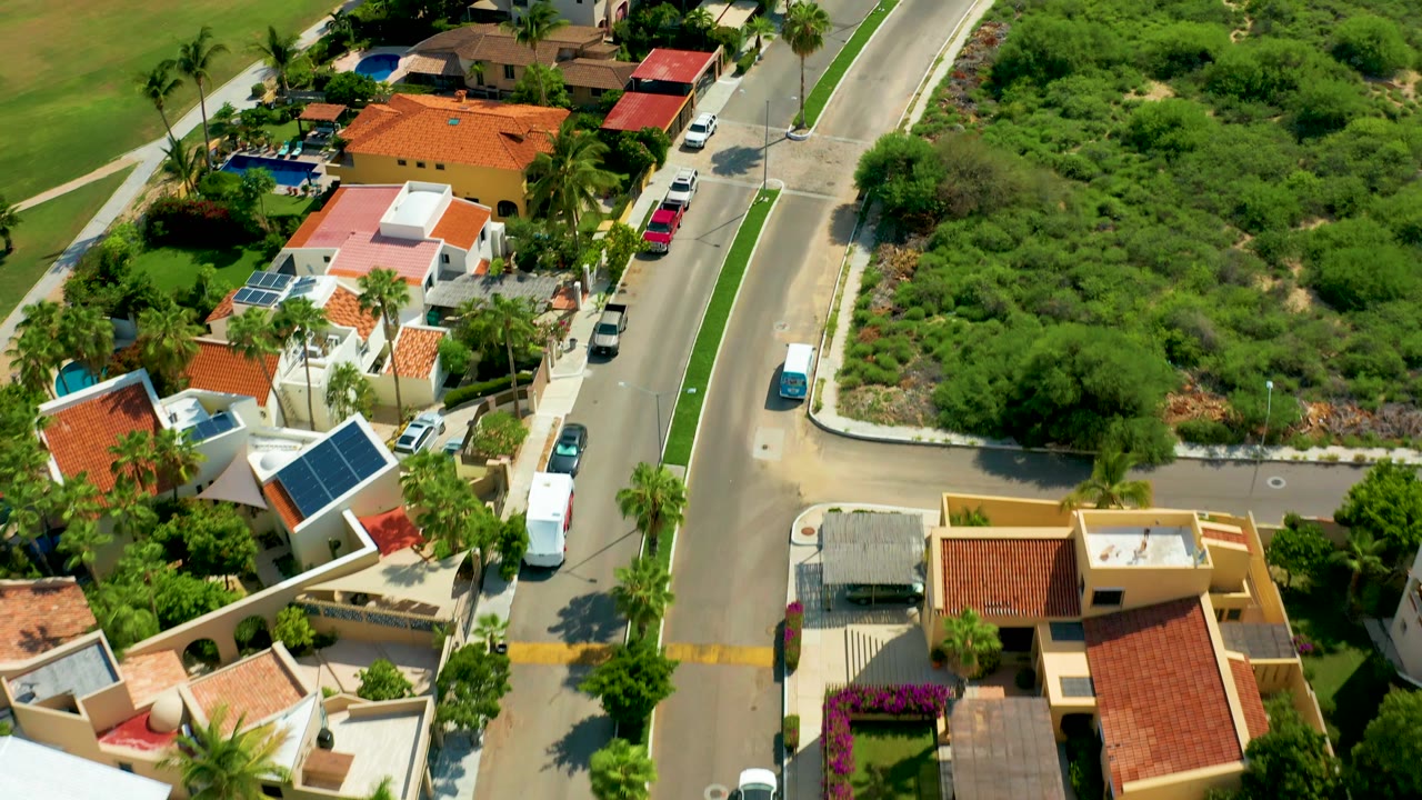 Drone view over houses with orange roofs and a road lined by vehicles.