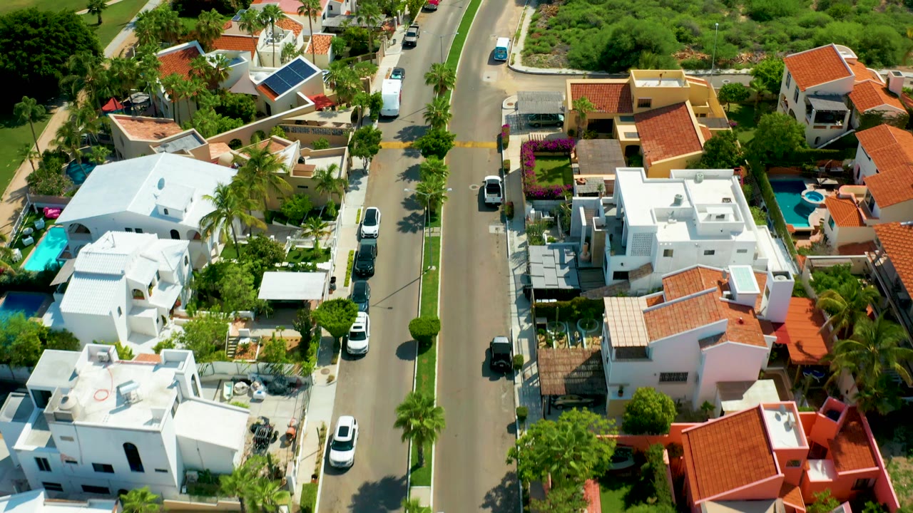 Drone view over a residential road lined with homes and greenery.