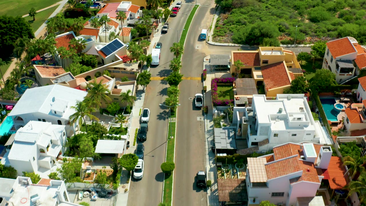 Aerial neighborhood frame with road, houses, palms, and a small pool.