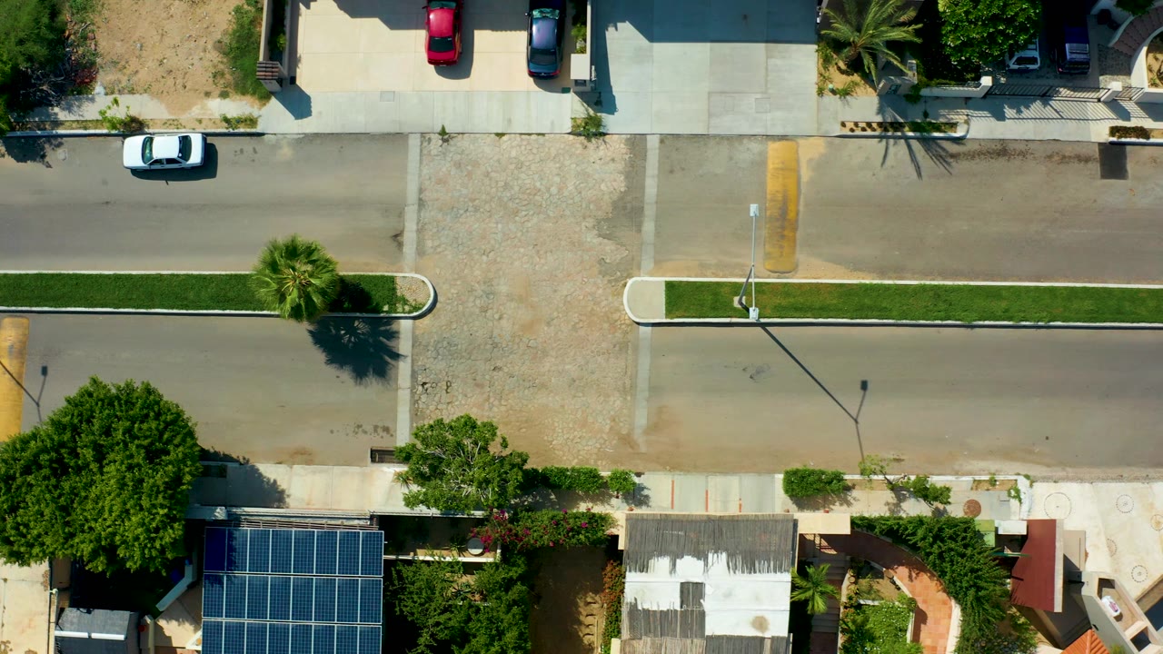 Overhead view of the same street as the white car moves along the road near homes and trees.