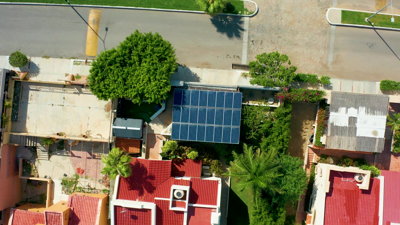 Overhead view in San Jose Del Cabo, Baja California Sur, showing a residential street, red-roofed homes, a blue solar panel array, palms, and no visible people at the start of the clip.