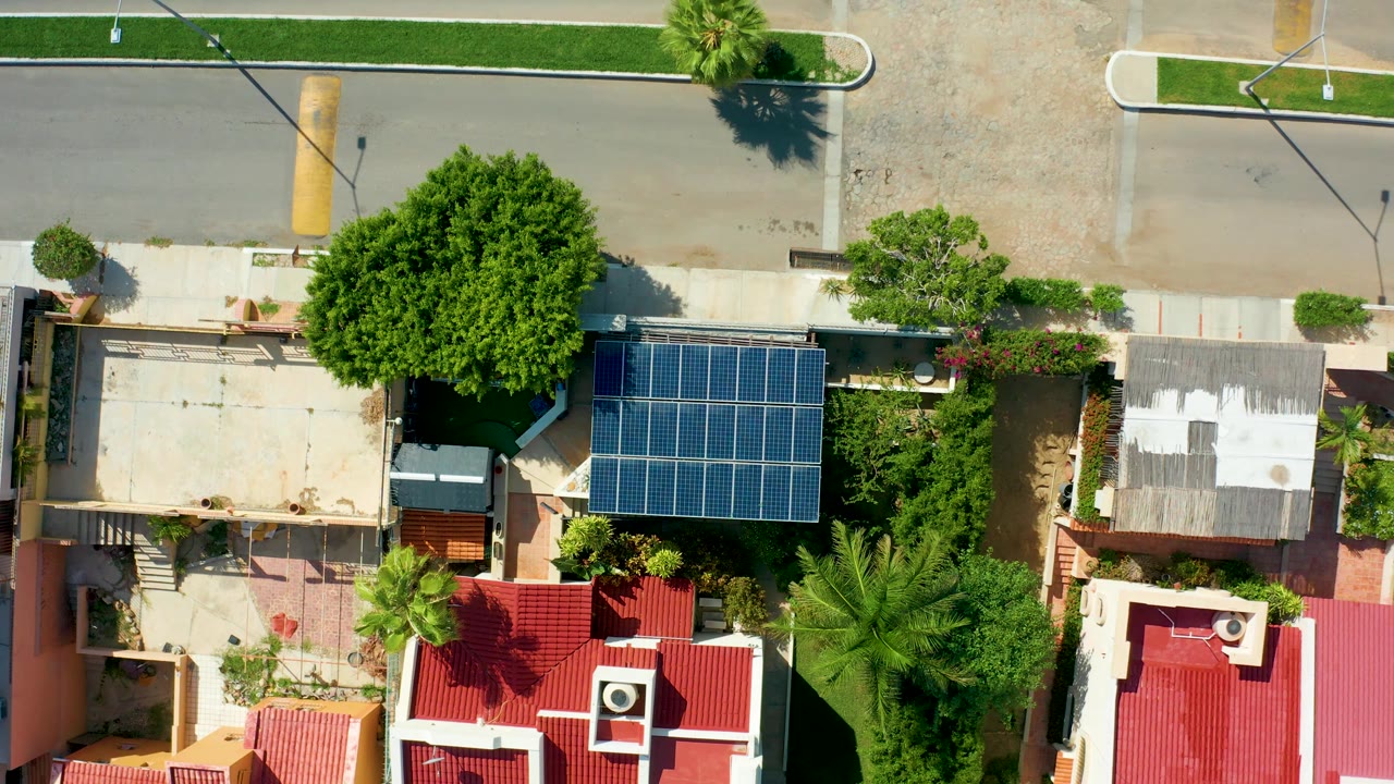 Overhead residential street scene with solar panels, red roofs, and dense trees.