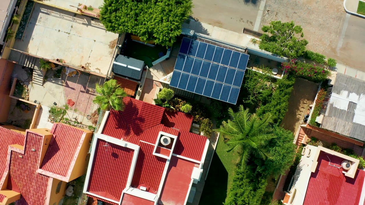 Top-down neighborhood view with solar panels beside red roofs and thick greenery.
