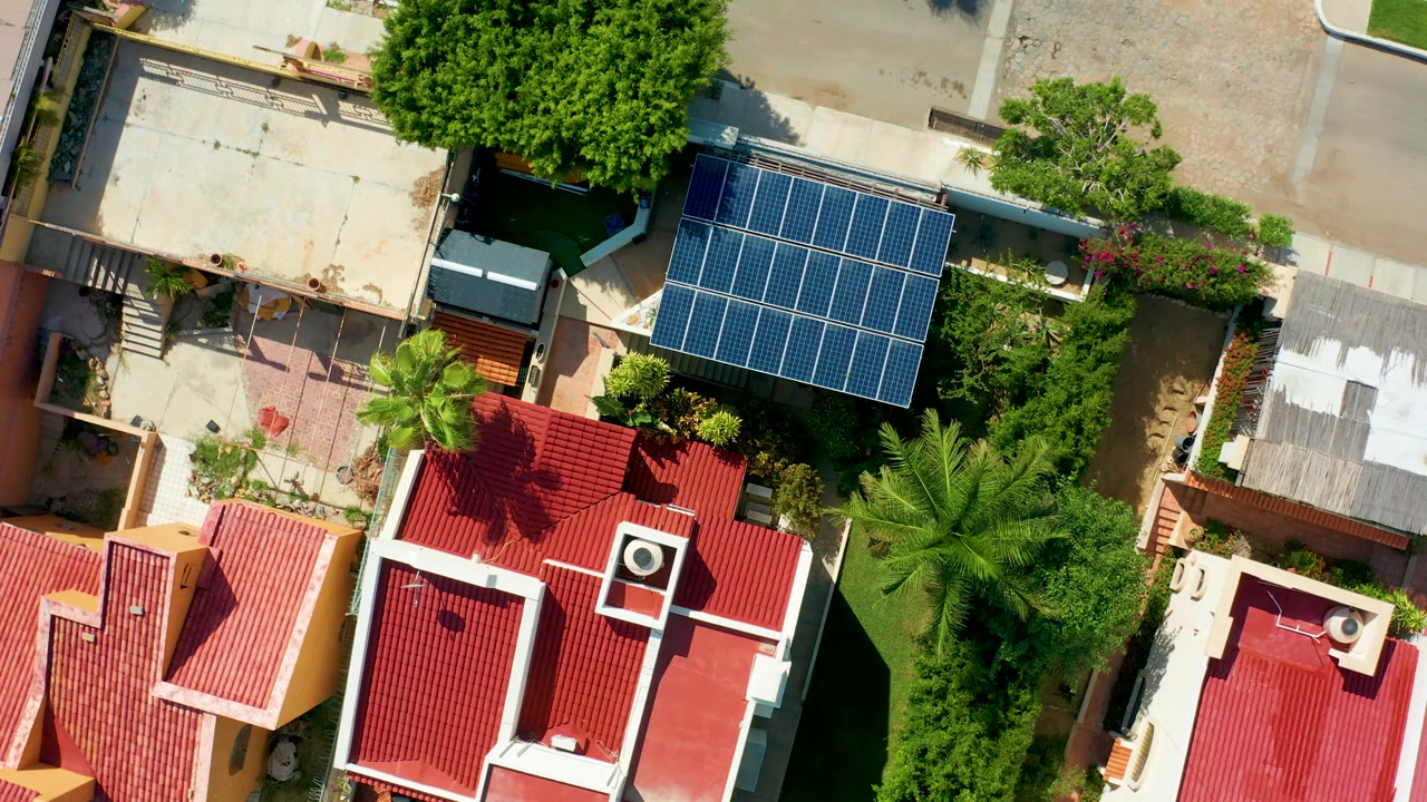 Overhead San Jose Del Cabo view with the blue solar panel array, red roof sections, a large round tree near the street, and no visible people.