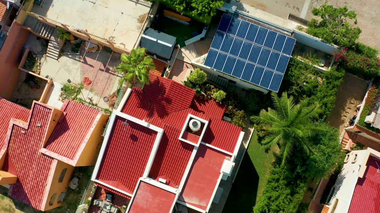Overhead angle on red roofs, solar panels, palms, and a pale paved area.