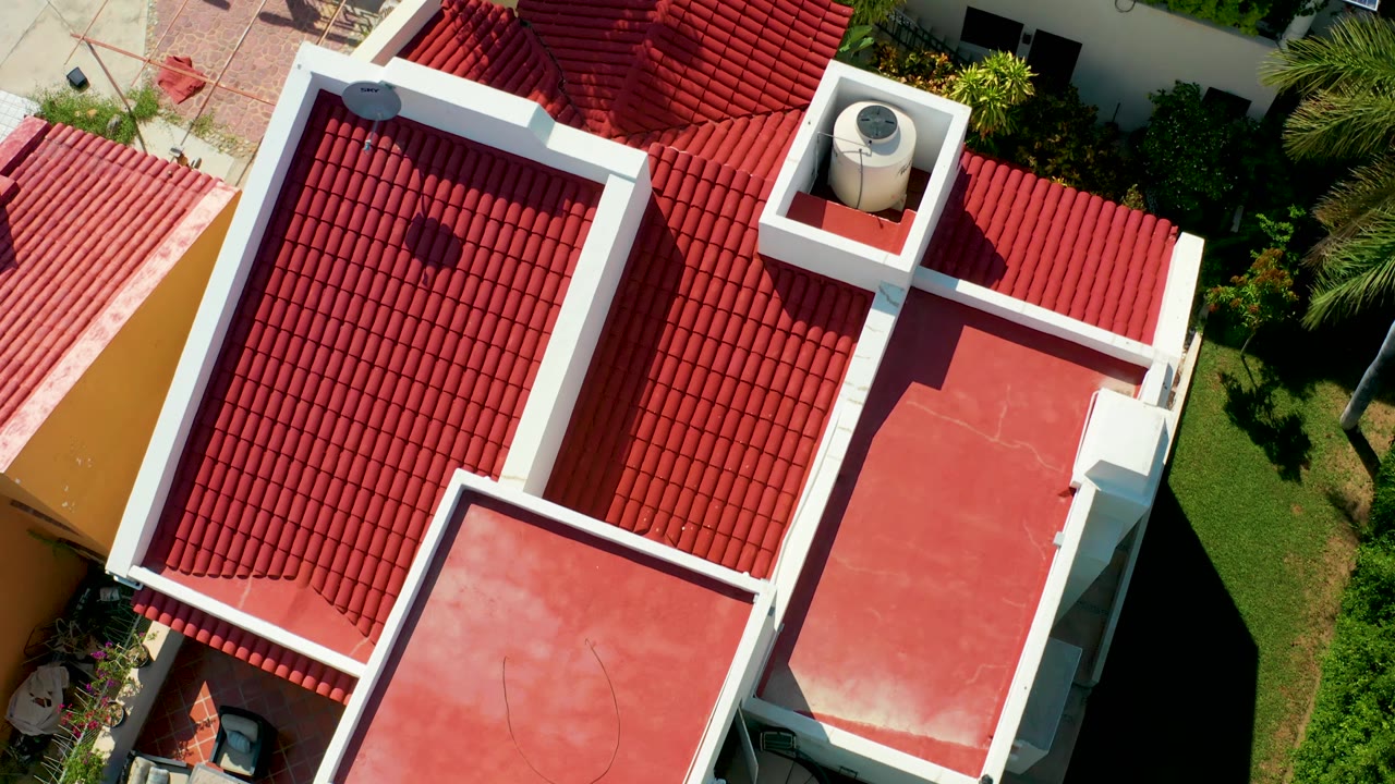 Overhead San Jose Del Cabo rooftop view where red tile roofs and white trim dominate the frame while a solar panel begins to appear near the upper right edge, with no visible people.