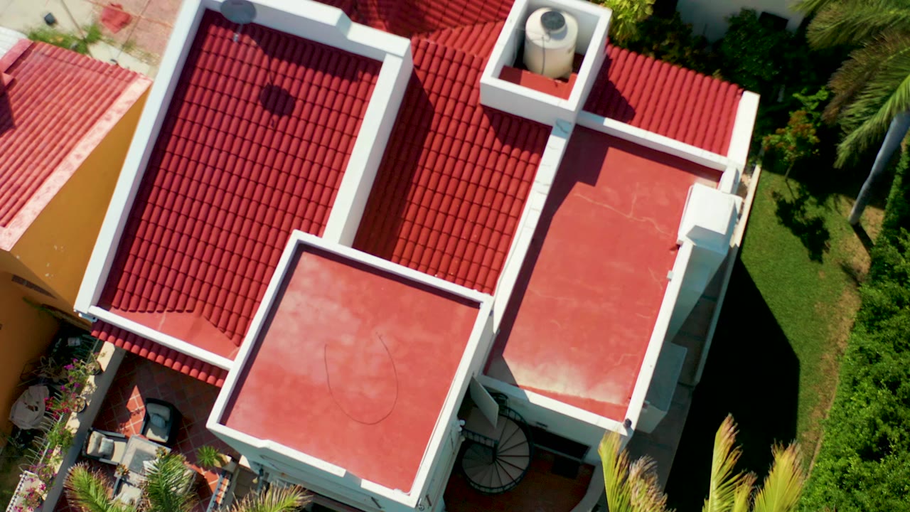 Overhead San Jose del Cabo frame showing red tiled roof sections, white parapet walls, flat red roof areas, surrounding greenery, and no visible people.