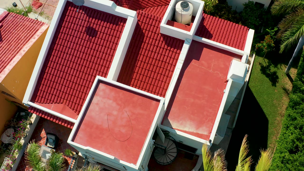 Top-down red roof building with a patio corner and greenery below.