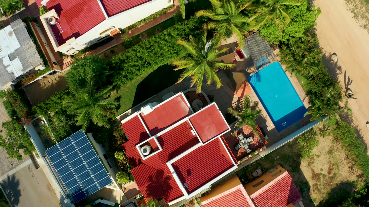 Overhead frame with solar panels, red roofs, palms, and the blue pool area shifted higher.