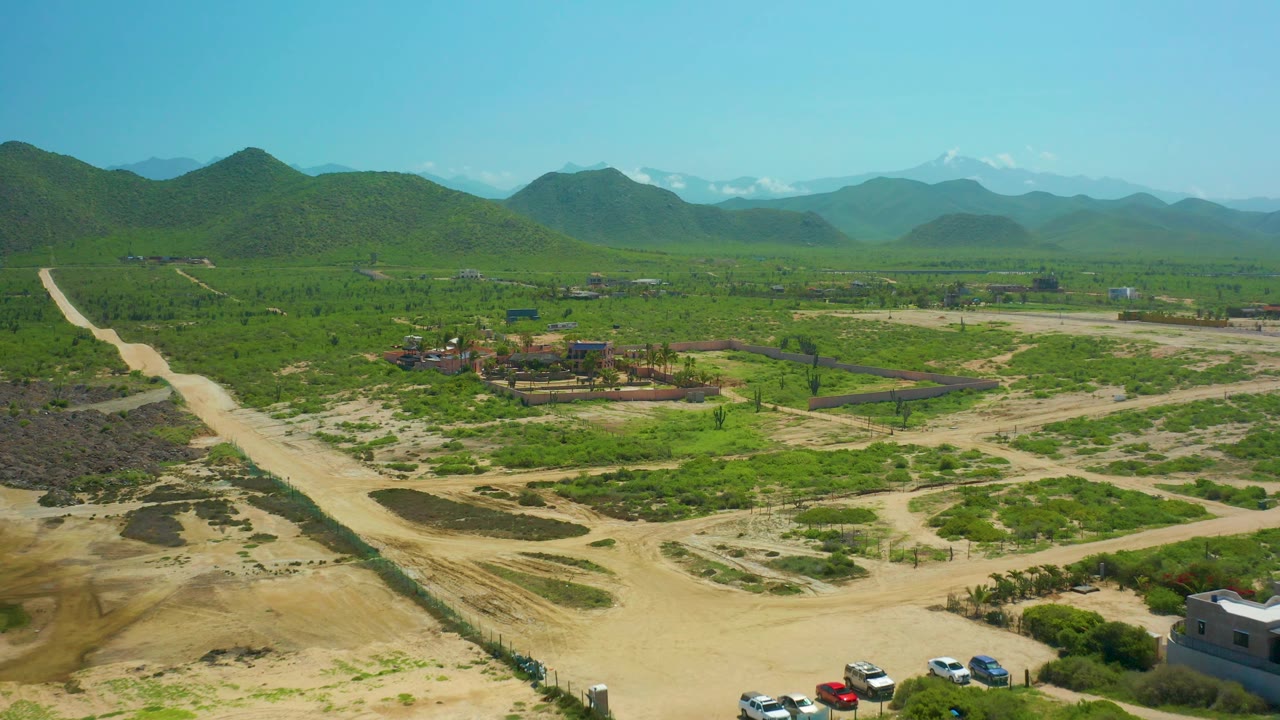 Aerial rural landscape with sandy roads, green vegetation, buildings, and mountains.