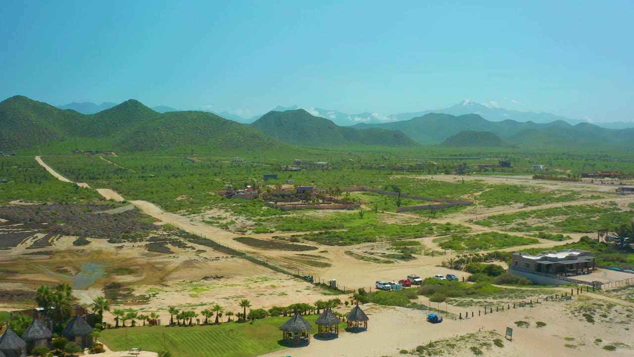 Aerial landscape with hills, green valley, dirt roads, small structures, and pool edge.
