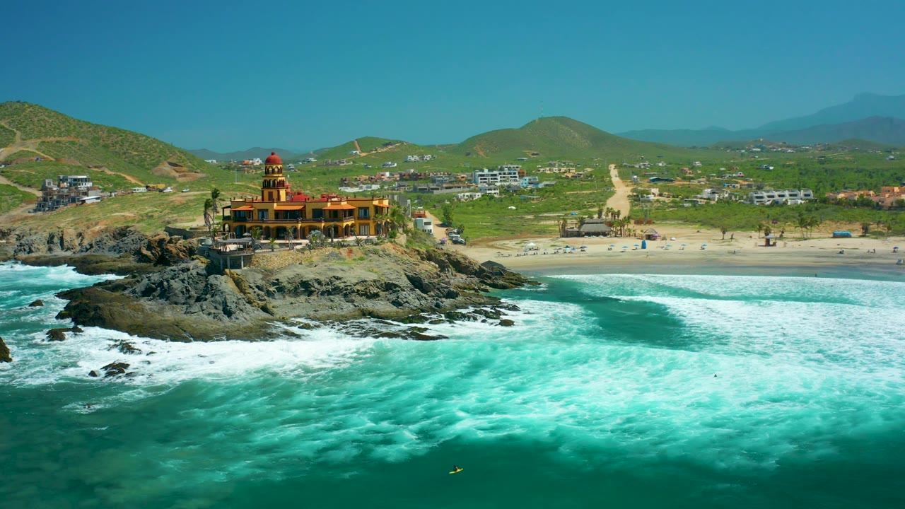 Rocky shoreline building beside foamy surf and sandy Cerritos Beach