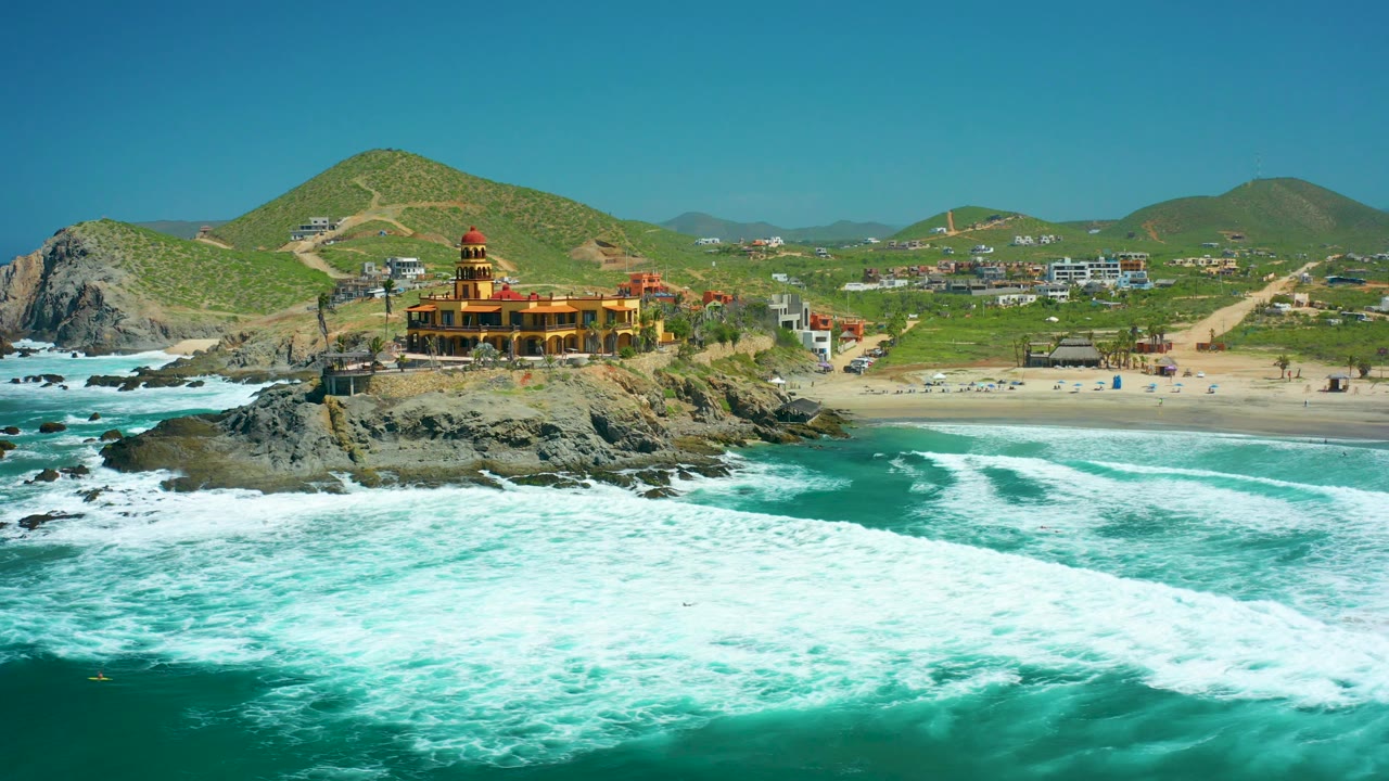 Drone view of waves breaking beside a rocky outcrop and beach settlement
