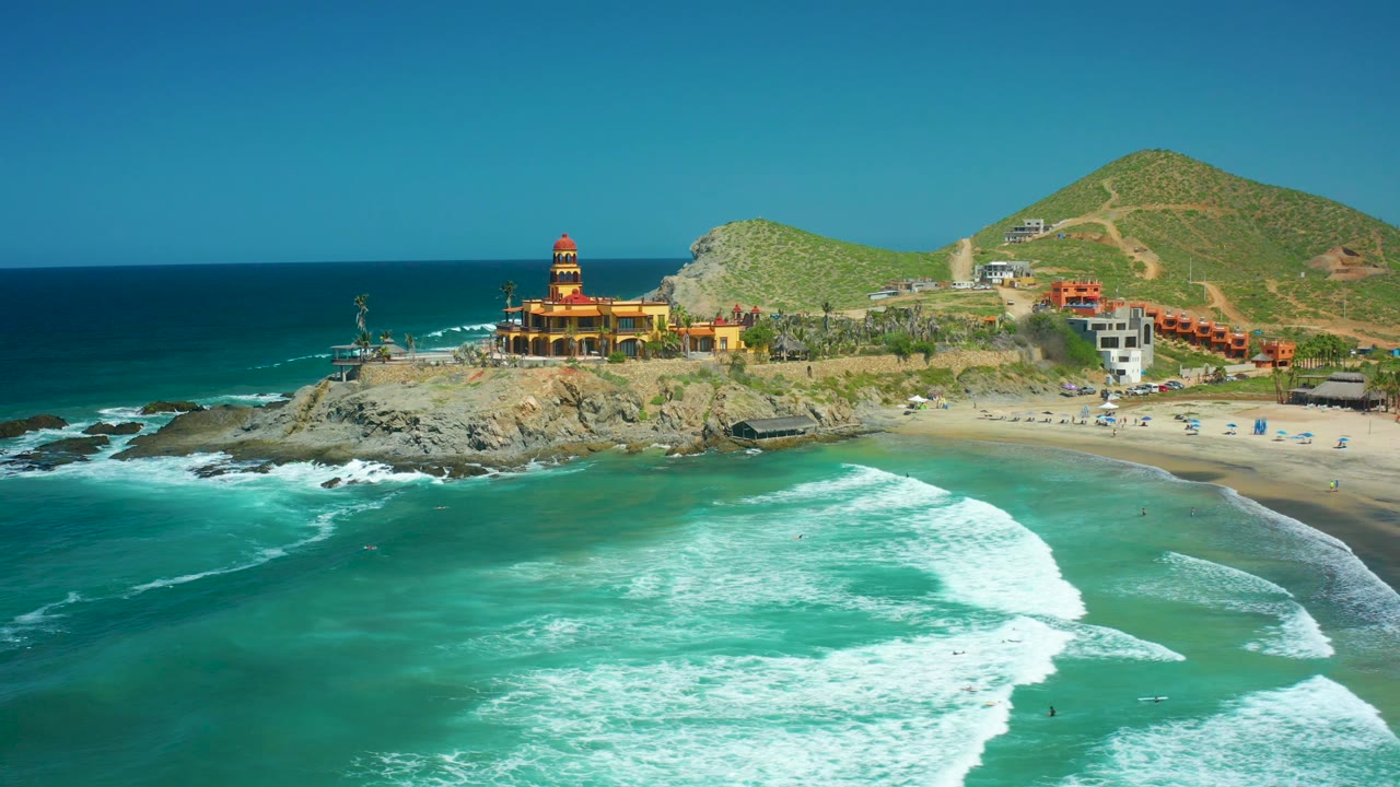 Aerial coastal view with lighthouse, rocky outcrop, beach, and rolling surf.
