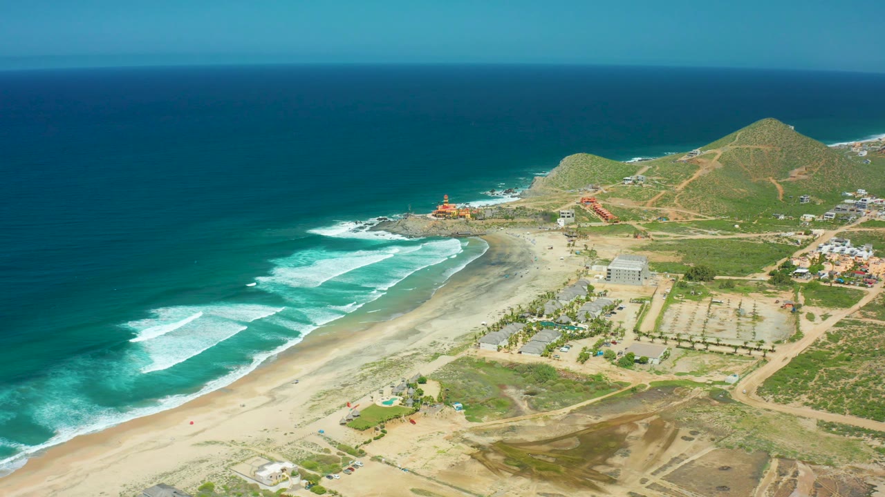 Aerial beach scene with breaking waves and a tiny red figure near the shoreline.