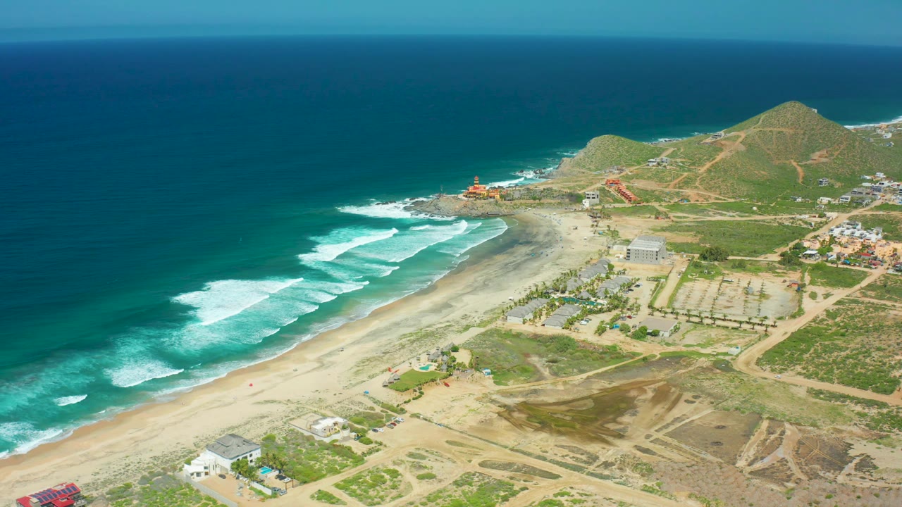 Third frame over Cerritos Beach with surf breaking diagonally along the sand, hillside paths in the background, scattered developed lots, and no visible people.