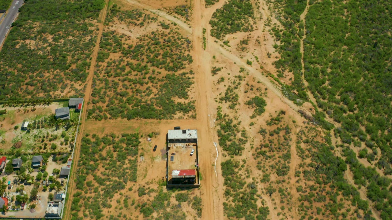 Top-down aerial view near Cerritos Beach, Baja California Sur, with tan dirt roads crossing green scrubland, a small building, parked vehicles, and no visible people.