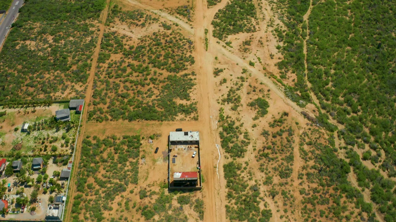 Aerial frame over Cerritos Beach area scrubland, showing intersecting tan tracks, a small building near the lower left, parked vehicles, and no visible people.